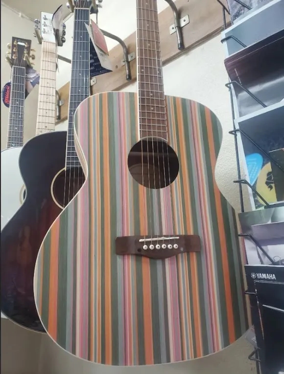 A row of guitars hanging in a shop, rainbow striped guitar at the front